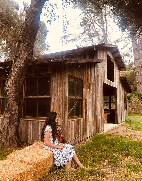 Teenage girl violinist sitting on hay bails in front of a barn