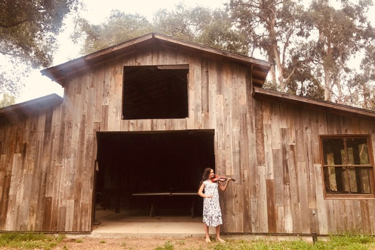 Teenage girl violinist playing in front of a barn