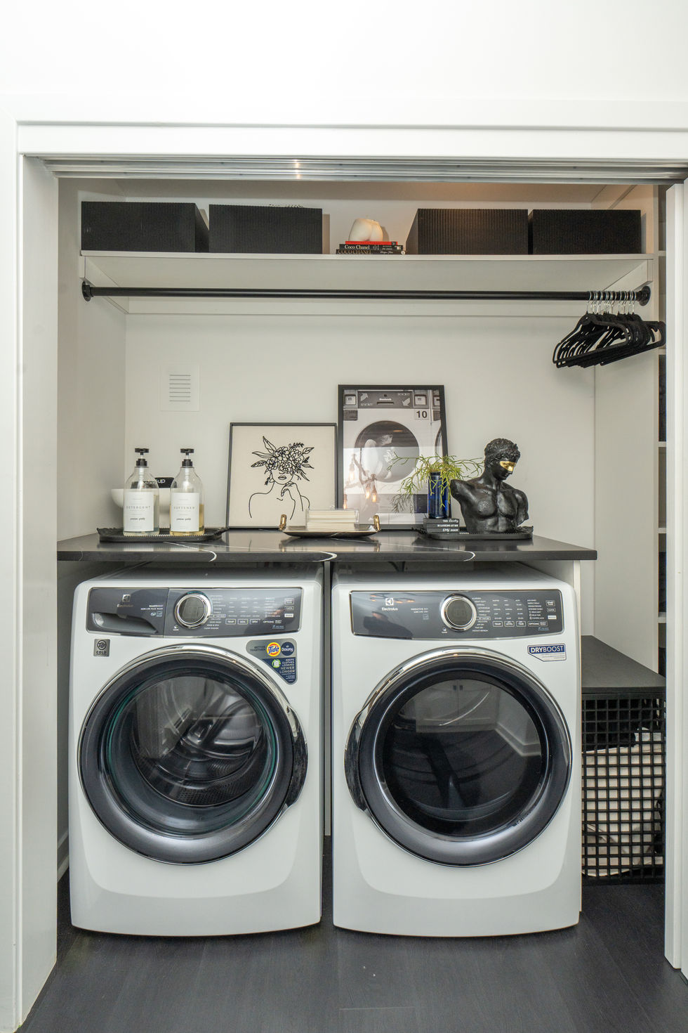 Modern laundry room with white washer and dryer, black countertops, shelves.