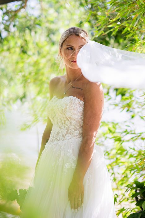 Braut mit wehendem Schleier im Sonnenlicht zwischen Blättern – Brautportrait Hochzeitsfotograf Berlin