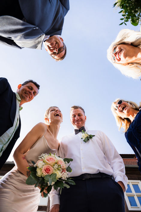 Brautpaar und Gäste lachen in die Kamera von unten – kreatives Gruppenfoto Hochzeit Berlin