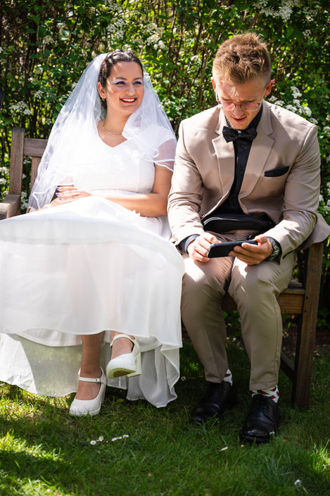 Brautpaar sitzt entspannt auf einer Bank im Garten – authentische Hochzeitsmomente Berlin