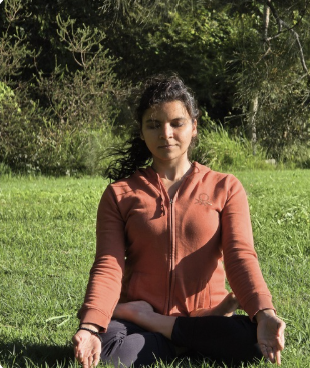 Sneha meditating cross-legged on the grass among trees