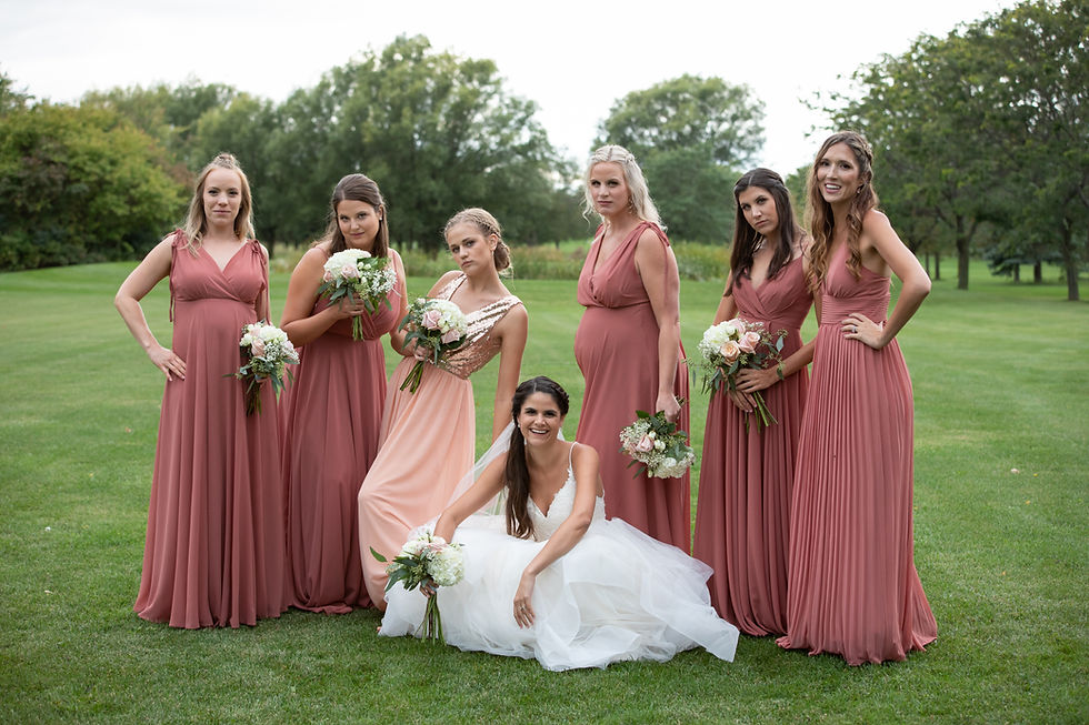 Bride and her bridesmaids striking a pose on the greens of a golf course with trees in the background. The girls are in various shades of pink. From light pink to rose pink. London Ontario Wedding Photography Lori Beneteau Photography