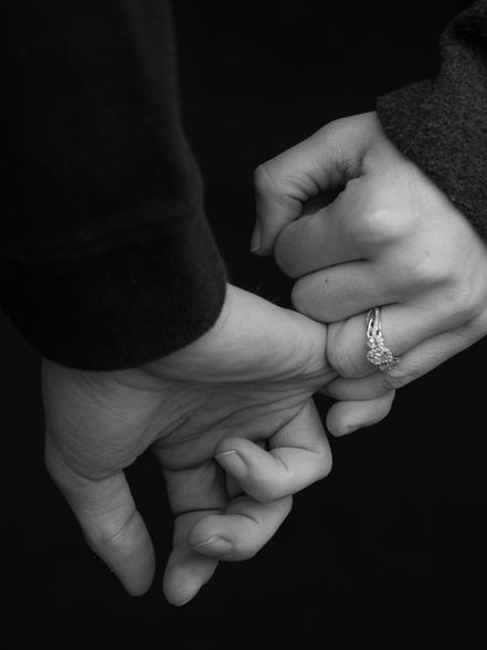 A black and white photo of a man and woman holding hands, and showing off the engagement ring.