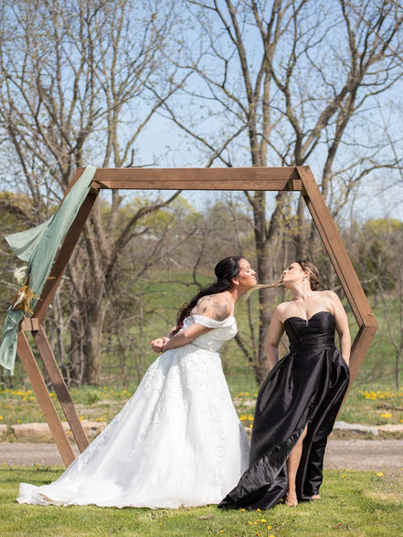 A bride and her bridesmaid having a funny moment blowing kisses at each other under the wedding arbour.