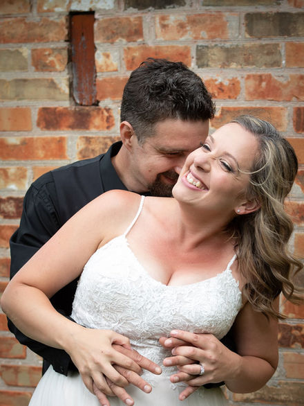Bride and groom standing together infront of a brick wall and laughing.