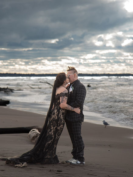 Stormy clouds on the beach with strong waves behind the bride and groom. The bride is wearing a stunning black wedding dress.