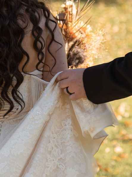 A close photo of the groom holding up the bottom of the bride's wedding dress as they walk away into the sunset.