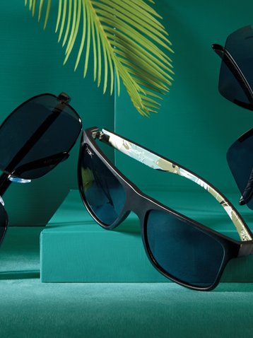 Luxury black sunglasses with green background and palm shadows—styled by Maria Lören for modern high-end fashion accessory campaign.