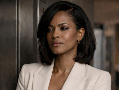 A high achieving female founder in a beige blazer stands thoughtfully in a dimly lit room, hands clasped, wearing a watch. The atmosphere is calm and professional. She is battling the internal struggle of burnout while trying to keep it all together.