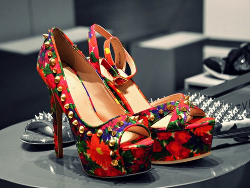 Bold floral platform stiletto heels with gold studs displayed in a luxury boutique setting, representing expressive identity, statement leadership style, and high-end women-centric branding aesthetics.