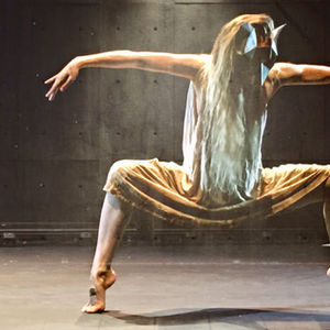a moody shot of a dancer crouched inn a box pose wearing a fox mask and dirty cream dress