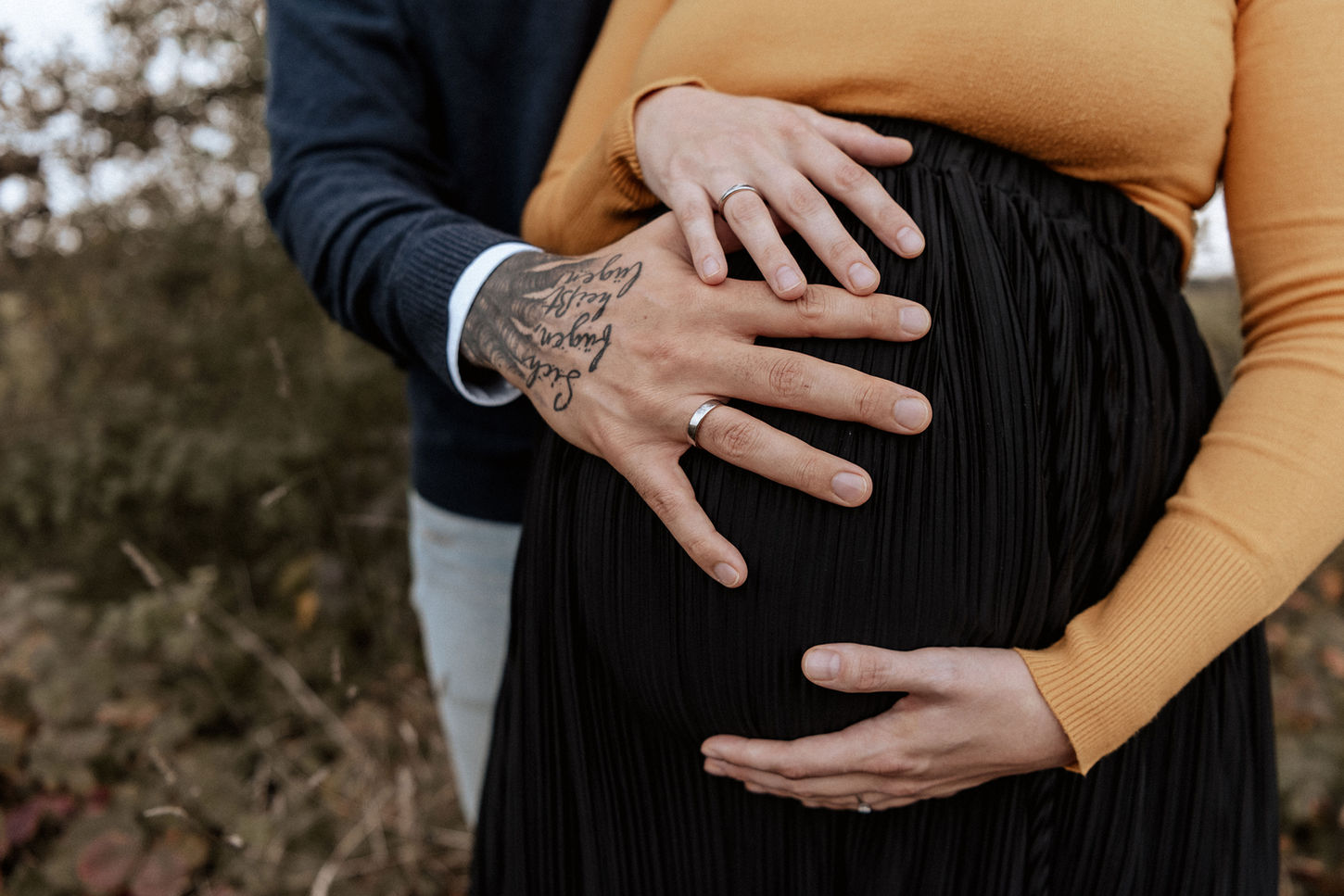 Babybauch und Familienfotos Olching. Detailaufnahme eines Babybauchs. Mama und Papa haben eine Hand auf dem Bauch