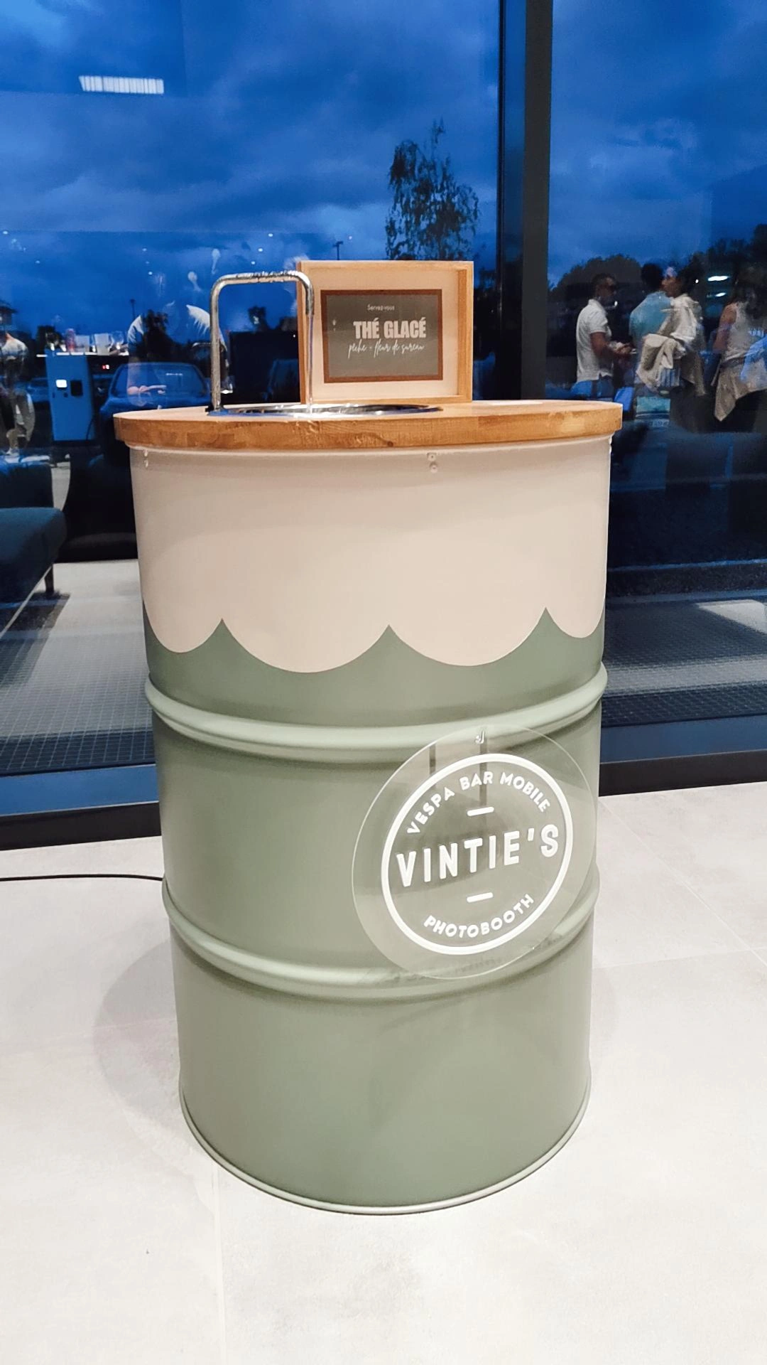 Tonneau en métal aux couleurs Vintie’s avec un plateau en bois, utilisé comme support pour un bar mobile ou une station de dégustation lors d’un événement en intérieur.