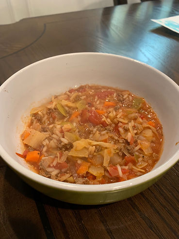 A white bowl filled with a colorful vegetable and rice stew sits on a dark wooden table. Bright tomatoes, carrots, and greens are visible.