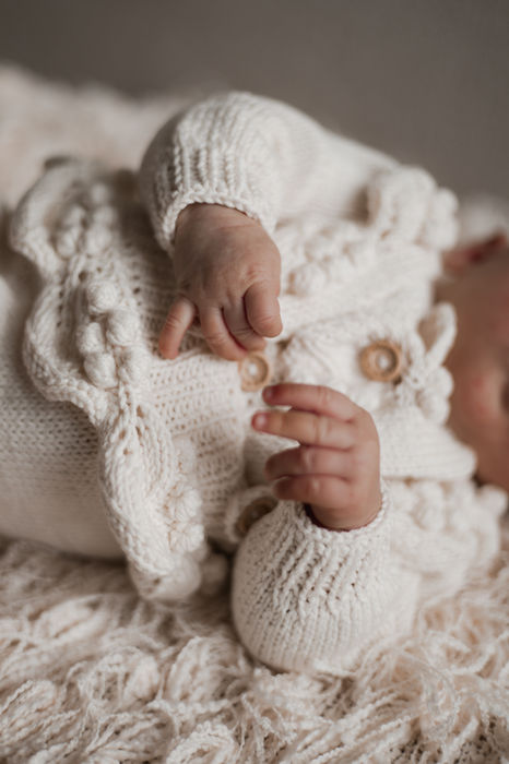 Foto van dichtbij van een pasgeboren baby. De handjes zijn in beeld en de baby heeft een gehaakt jasje aan. 