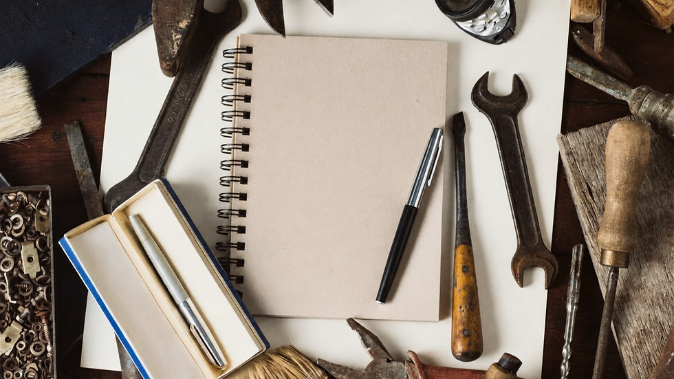 Blank spiral notebook with pen, surrounded by worn hand tools and brushes on a rustic workbench, creating a craftsman mood