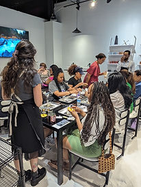 Group of women craft together at a table in a brightly lit studio setting.
