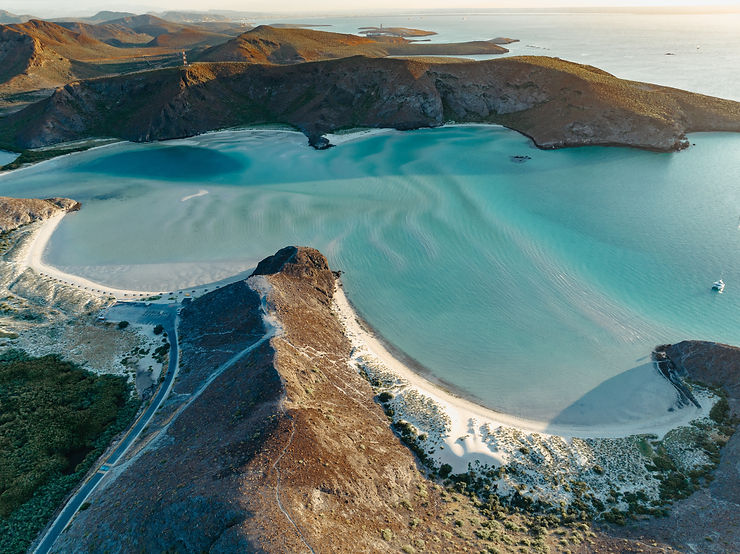 drone shot of white sand blue water beach with mountains