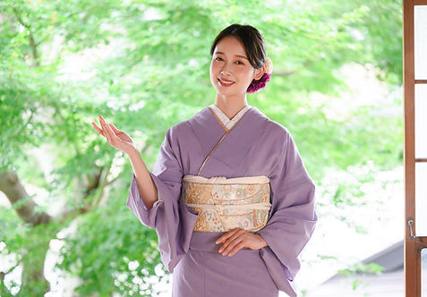落ち着いた紫色の着物を着て手を差し出し着付け屋 着楽の着付け教室を案内している女性
