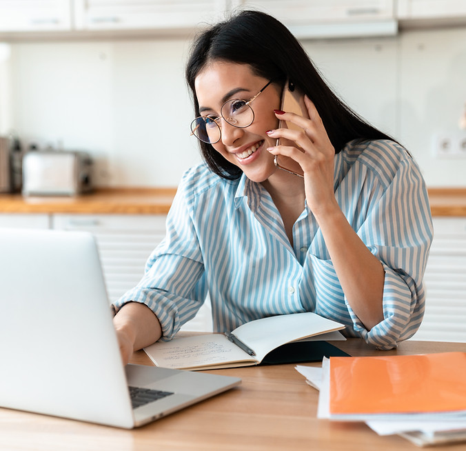 Woman wearing glasses, looking at a laptop, and talking on the phone