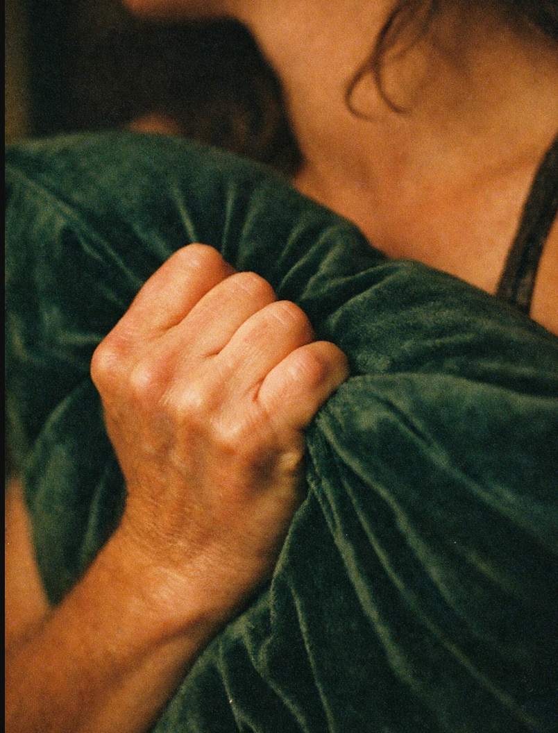 A person holding a soft green velvet pillow tightly against their chest, creating a cozy and calm mood.