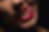 Close-up of a person's mouth with bold red lipstick. They are playfully licking their upper lip, showing white teeth. Dark background.
