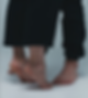 Two pairs of feet, one on tiptoe, in black pants on a light floor. The scene conveys intimacy and balance. No text present.