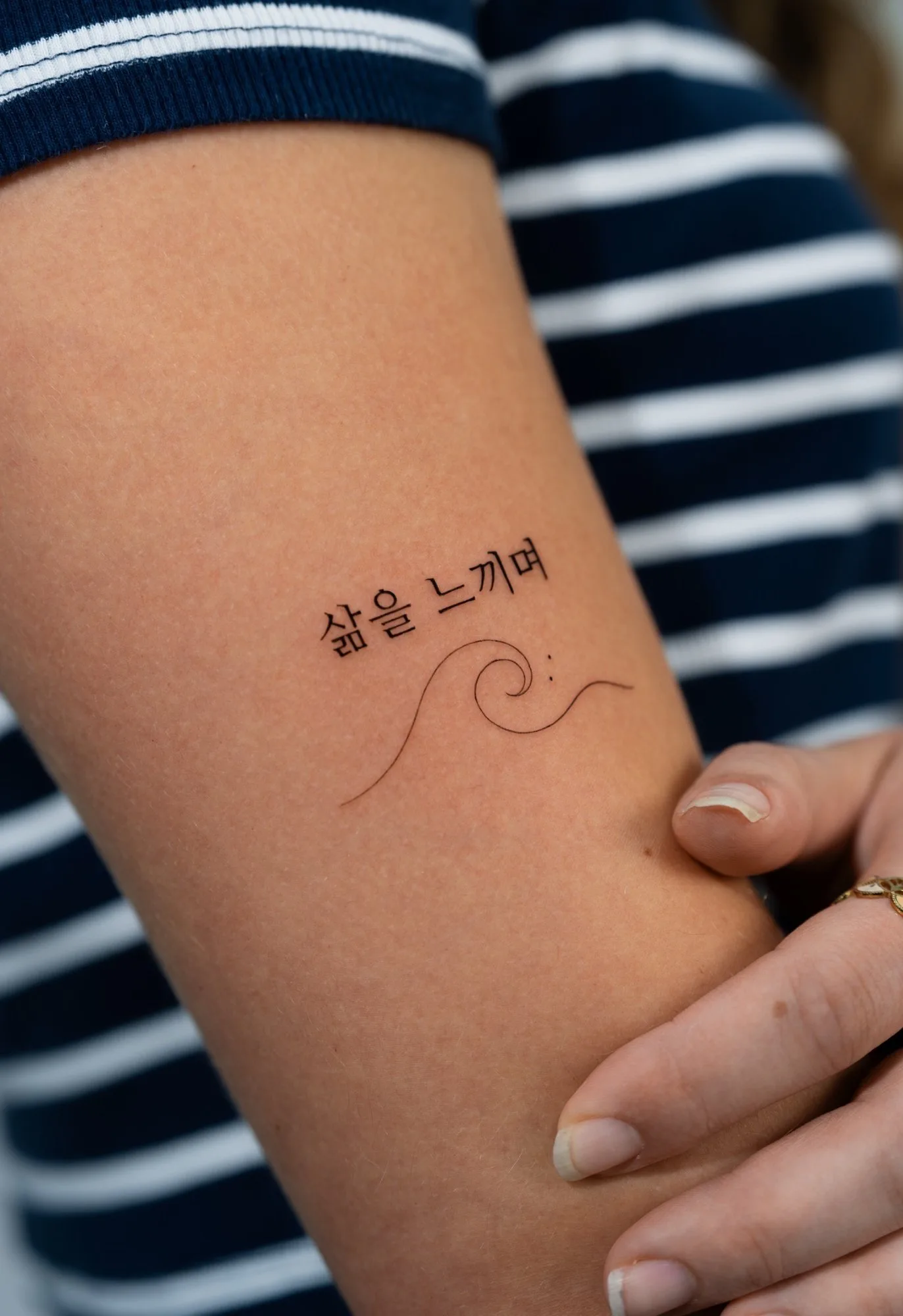 Fineline tattoo on the arm featuring the Korean phrase '삶을 느끼며' (meaning 'feeling life') above a minimal single-line wave. Seoul Ink Tattoo, Gangnam, Seoul, South Korea.