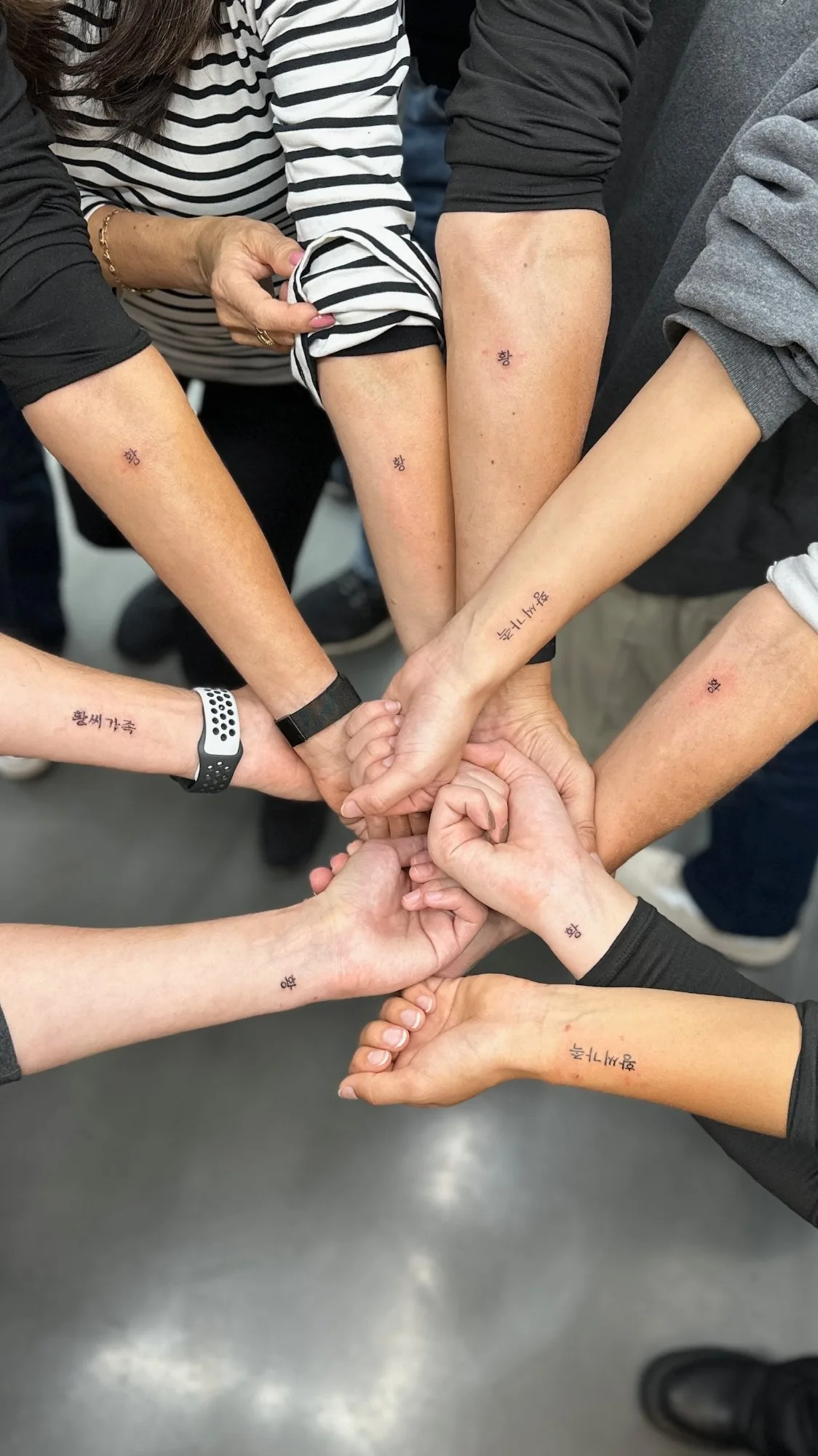 Group photo of a family showing matching minimalist Korean Hangul lettering tattoos on five wrists and forearms gathered together in a circle. Seoul Ink Tattoo, Gangnam, Seoul, South Korea.