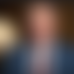 Official portrait of Minnesota Governor Tim Walz speaking, wearing a blue suit, white shirt, red tie, and American flag pin, against a formal indoor background with a lamp—Walz has faced criticism for oversight failures during the escalation of the state’s daycare fraud scandal under his administration.