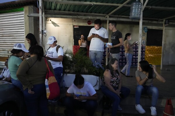 Families wait anxiously outside Caracas prison, using phones and showing emotion amid January 2026 political prisoner release hopes.