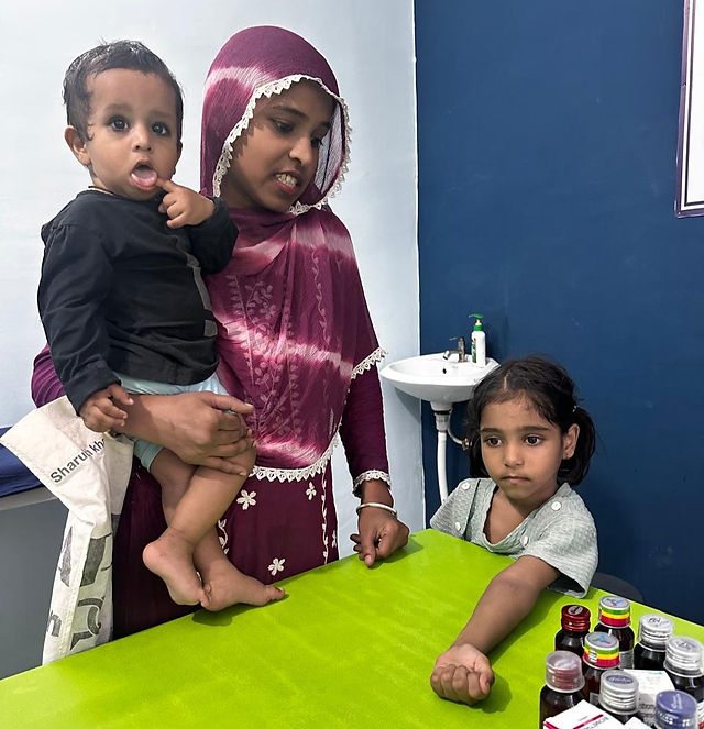 A young girl lays her arm on an examination table with her Mom and sibling nearby.