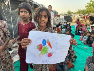An young girl shows her drawing of a bowl with fruits and vegetables.