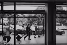 Ankommende Gaeste mit Koffer im verglasten Eingangsbereich des Bezirksamts Eimsbuettel, schwarzweiss.