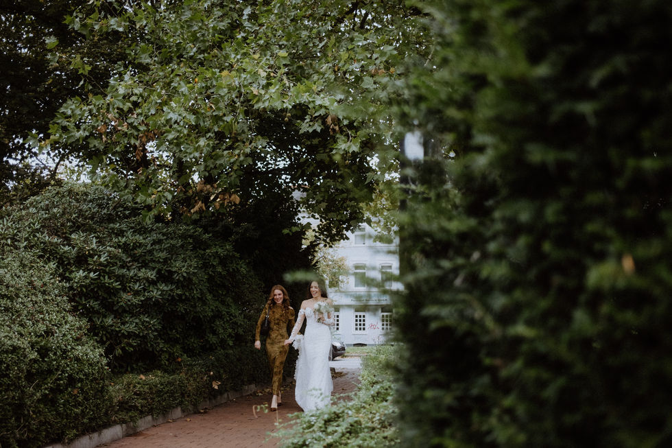 Braut geht gemeinsam mit Begleitung durch den Park Richtung Trauung.