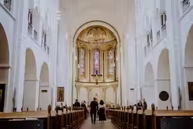 Heller Kirchenraum in Hamburg mit Mosaik am Altar und bunten Fenstern.