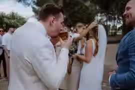 Bräutigam nimmt einen schluck nach der Trauung, während die Braut einen Gast umarmt