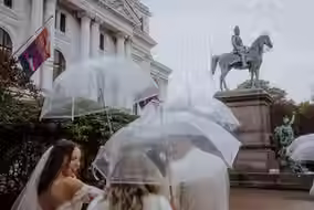 Brautpaar mit Gaesten und transparenten Schirmen vor weißer Säulenfassade in Hamburg.