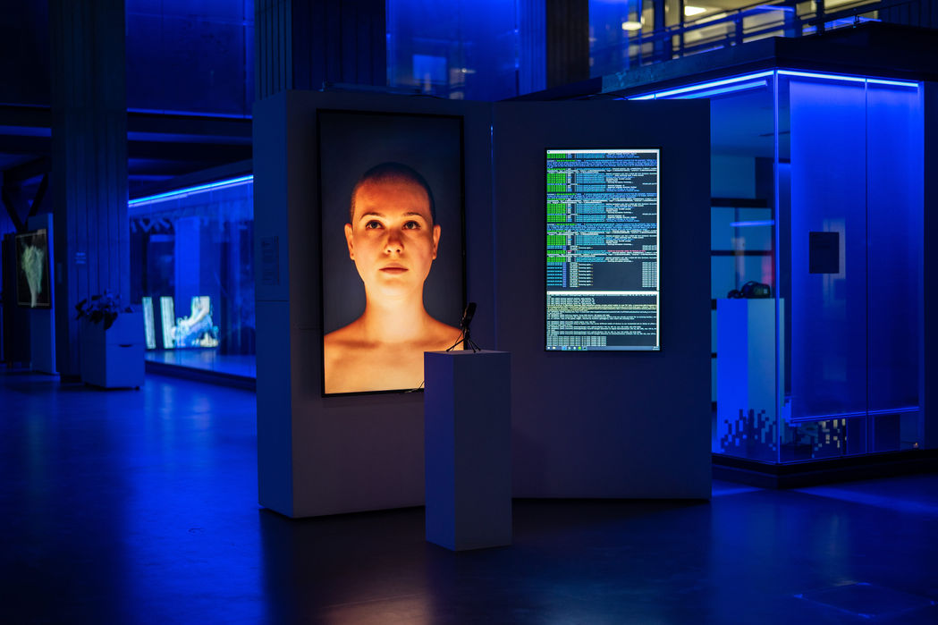 Wide blue hall with two avatars and data display: (Very) Neural System, immersive AI installation by Martina Pizzigoni