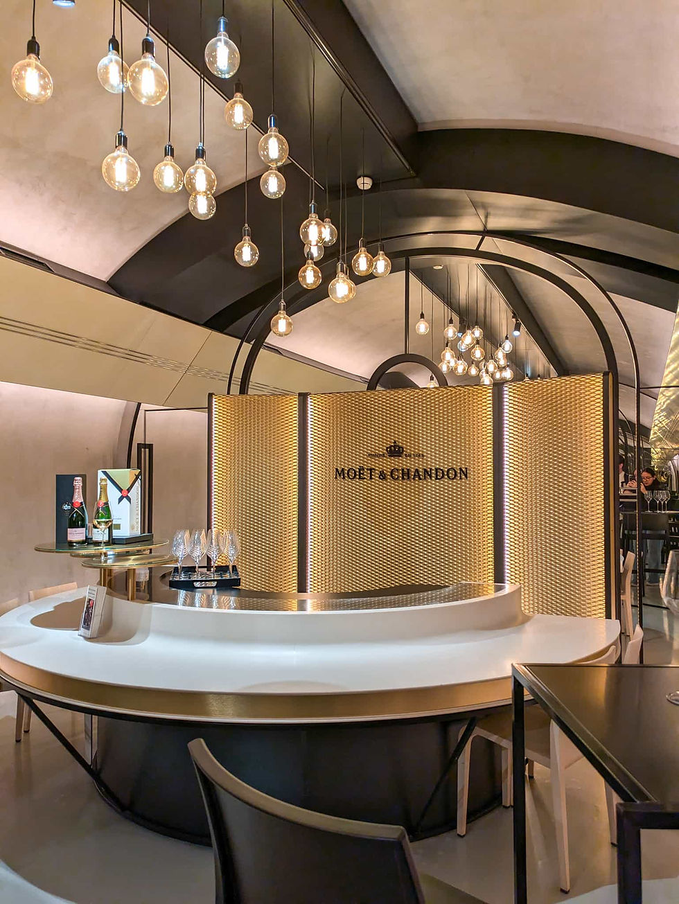 Champagne region France Reims Epernay Elegant Moët & Chandon tasting bar with glowing pendant lights, champagne bottles, and gold textured backdrop in a chic lounge.