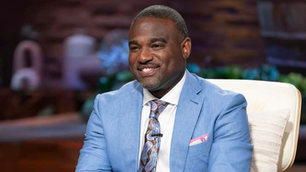 Venture capitalist Rashaun Williams smiling in a light blue suit while seated on the set of ABC’s ‘Shark Tank,’ where he appears as a guest investor.