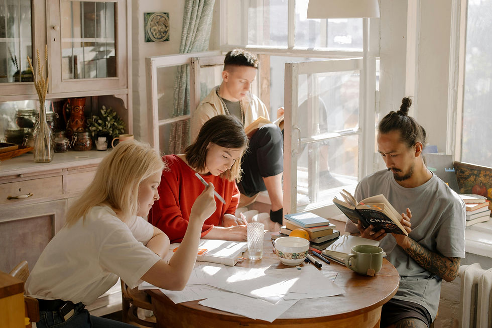 Four people in a cozy room, reading and writing at a round table. Sunlight streams through the window, creating a warm, focused mood.