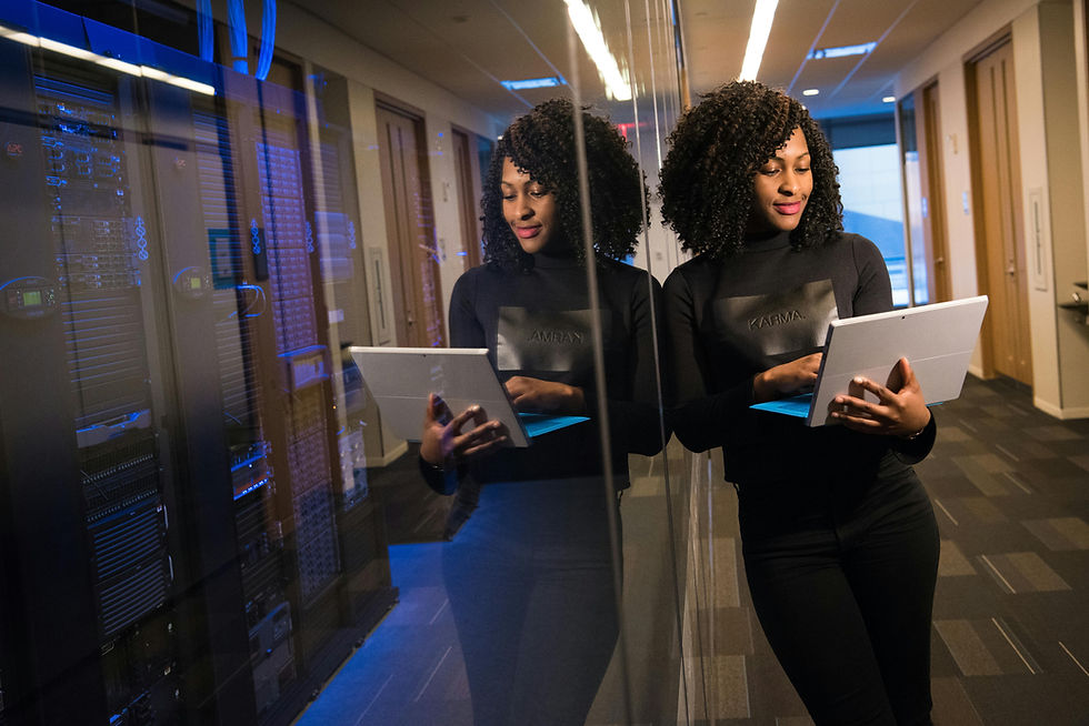 Woman in black holding a tablet in a server room, reflected in glass. Blue lights in the background create a tech-focused atmosphere.