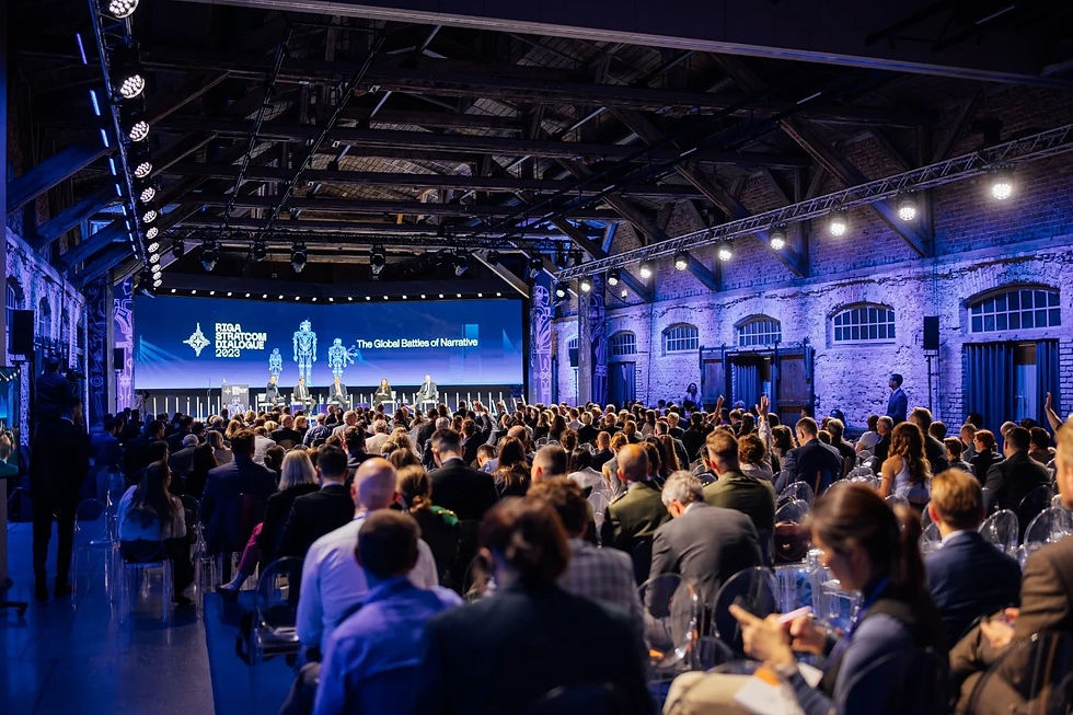 Large audience attending the NATO StratCom Dialogue conference, with a panel on stage discussing narrative warfare and strategic communication.