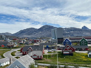 Vista di una città della Groenlandia con abitazioni colorate e montagne artiche sullo sfondo, esempio dei centri abitati che costituiscono il tessuto politico e sociale dell’isola.