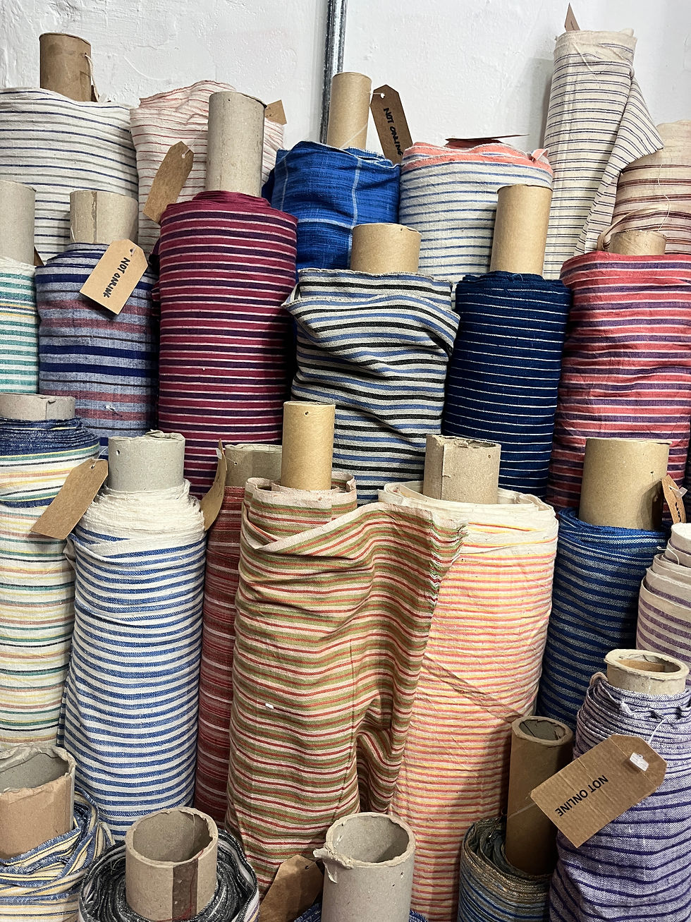 Rolls of striped fabric in different colours stacked closely together on cardboard tubes, with brown paper tags hanging from several of the rolls.