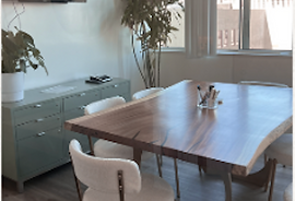Conference table made out of live oak with white chairs, sage green file cabinet, and tall green tree in corner.