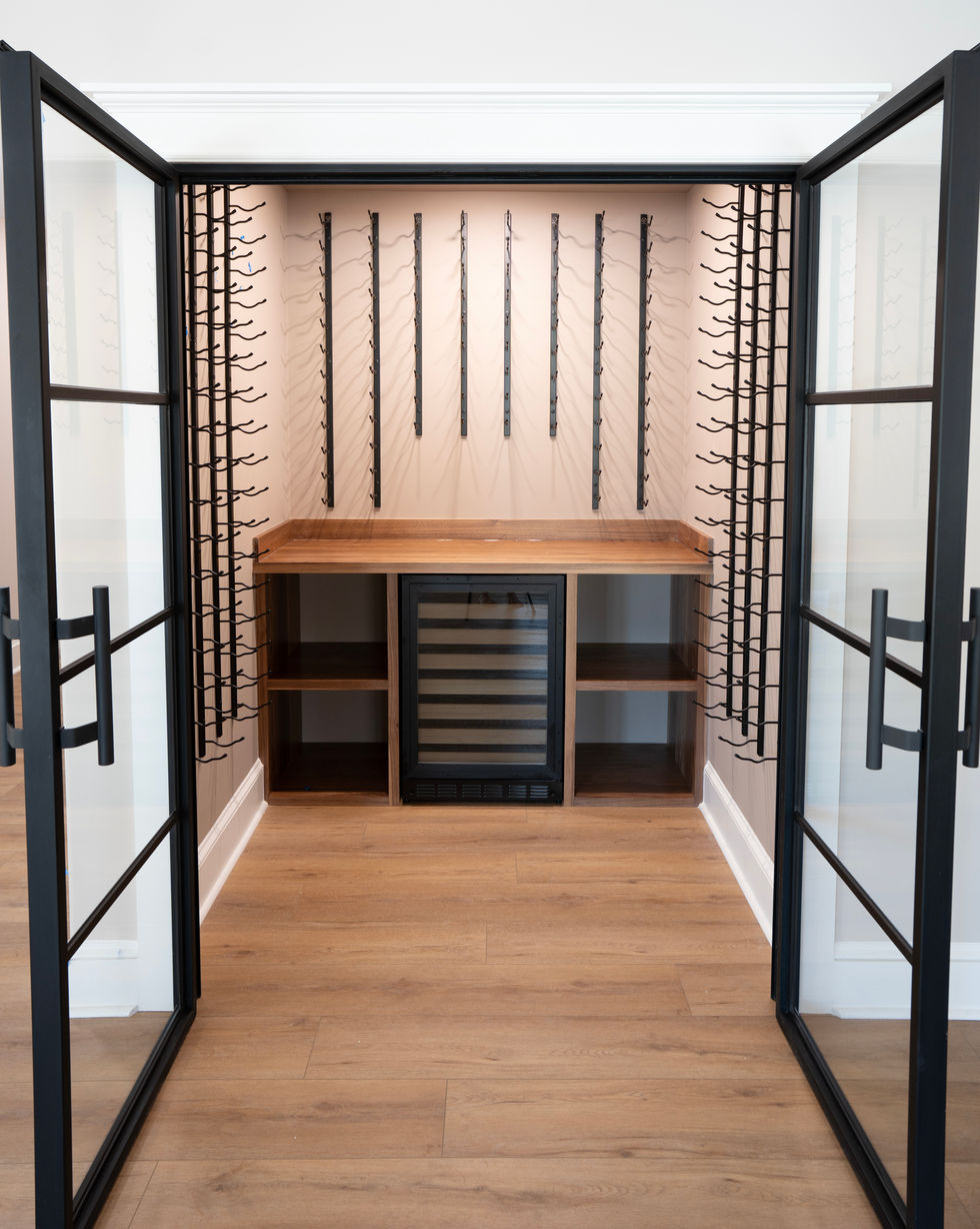 Modern wine room with black racks, wine fridge, wood countertop, and black framed glass doors.